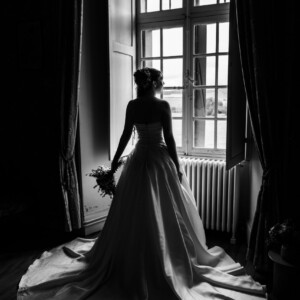 photo en noir et blanc de la mariée qui regarde par la fenêtre du château